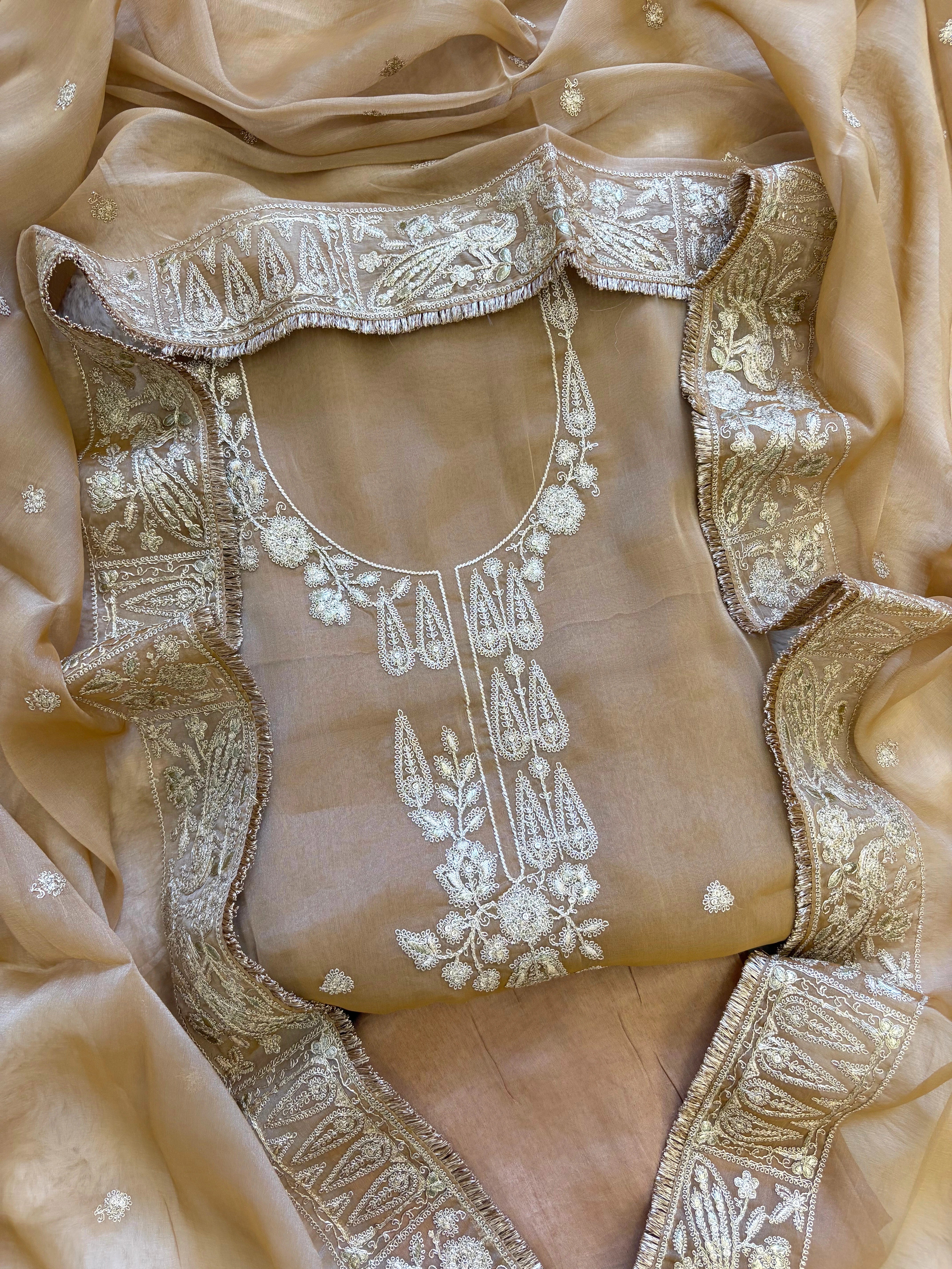 Beige organza unstitched suit with golden zari embroidery and embroidered dupatta, ideal for weddings and festive celebrations.